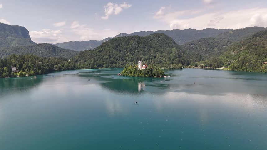 An aerial view of a church on an island in the middle of a lake surrounded by greenery and mountains