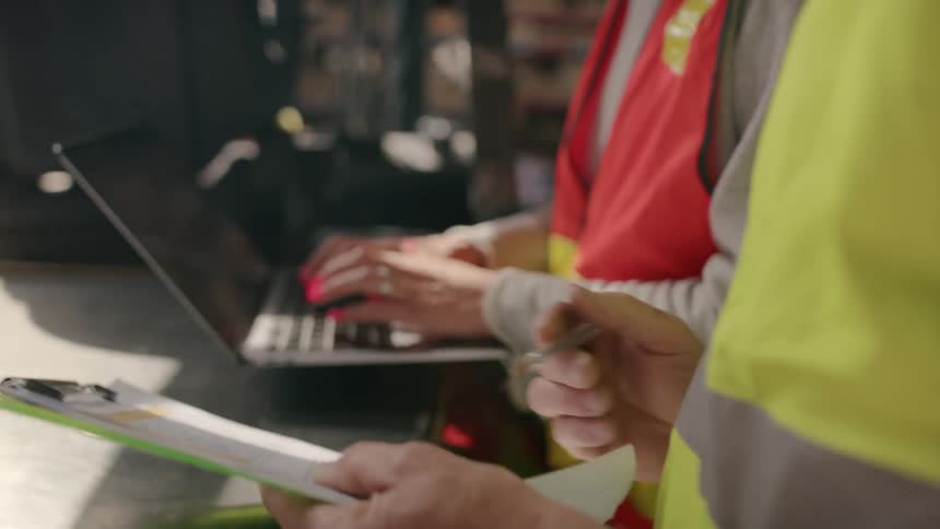 Hands of two people side by side talking with one of them writing on a document and the other typing on a laptop