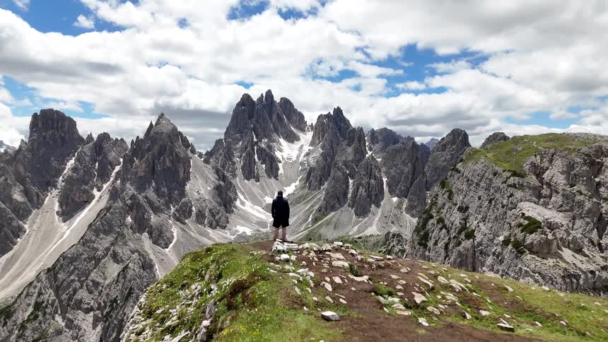 Man stands at the edge of a cliff and stares at the enormous mountains across the canyon