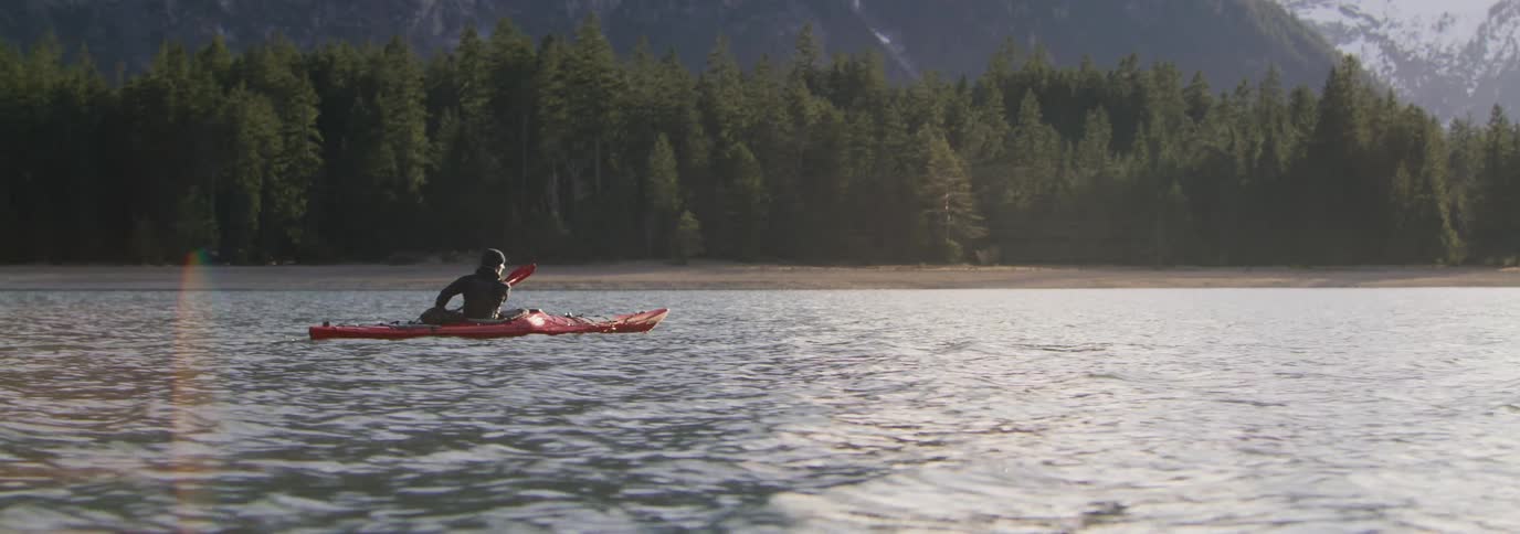A person in a red kayak on a lake and he is paddling sideways