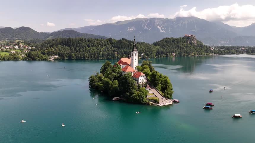 Aerial landscape of a church on an island surrounded by a blue lake and mountains on the horizon