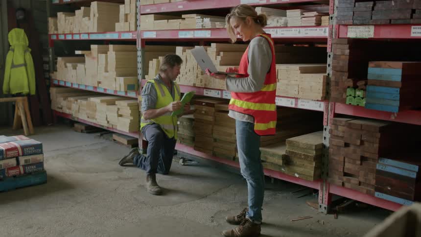 Man and woman taking inventory of lumber on a clipboard and a laptop computer