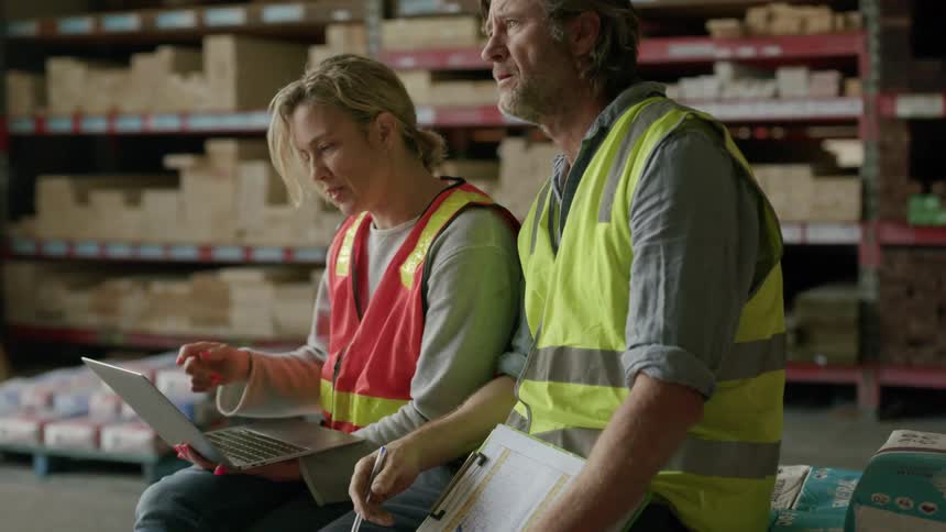 Two workers with vests sitting debating in a storage center