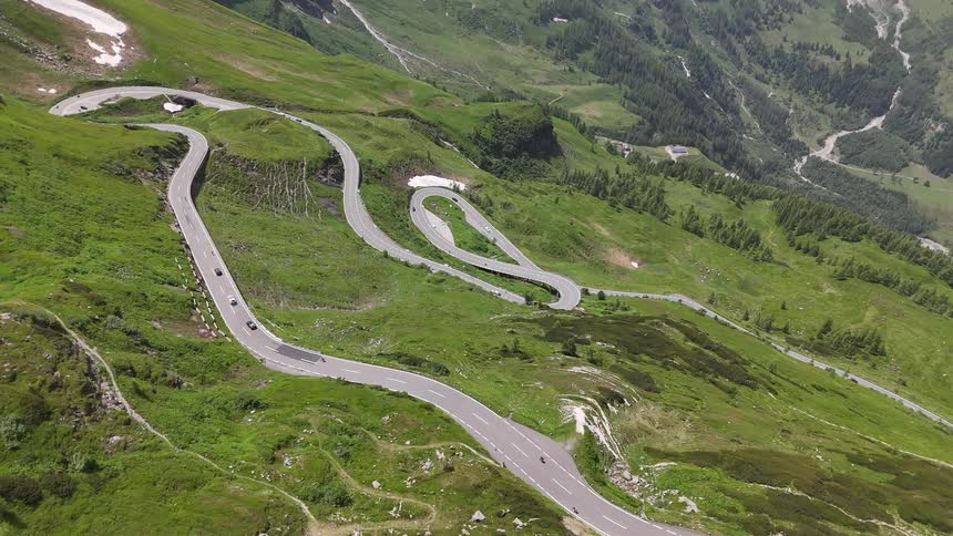 Aerial scenery of a road winding up the greenish mountain with vehicle traffic