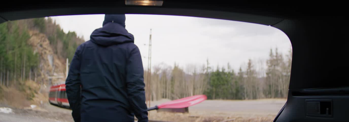Man taking a paddle from a kayak inside a car and a train passing in the background