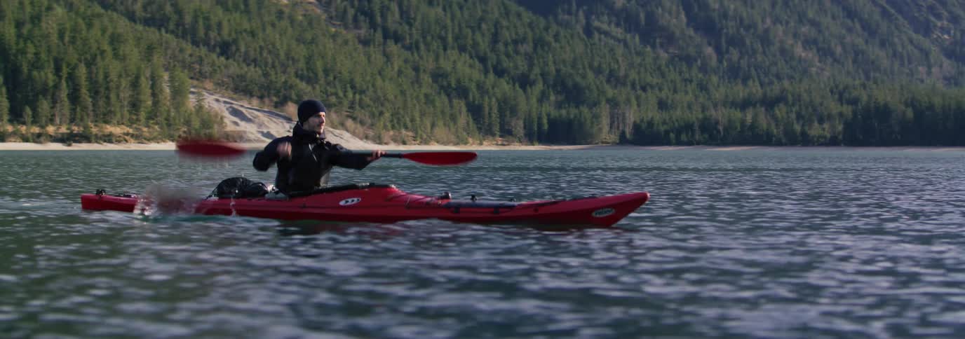 Man paddling a red kayak on a lake with mountains and trees in the background