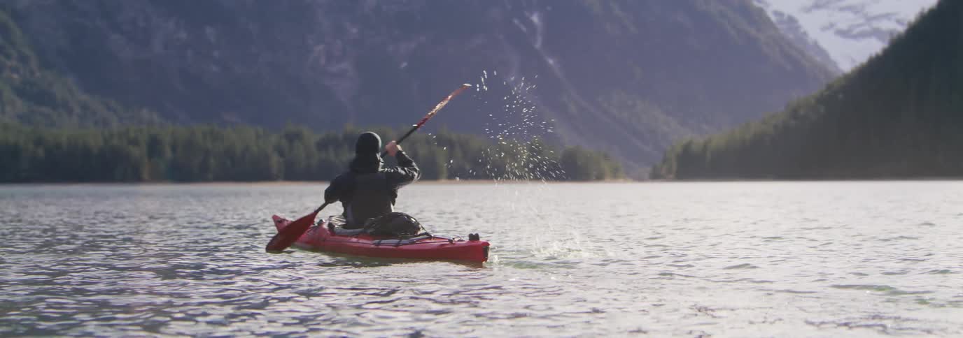 Man paddling a red kayak in calm waters with sun glare