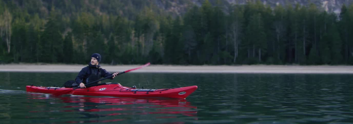 A man in warm clothes is in a red kayak on a large lake
