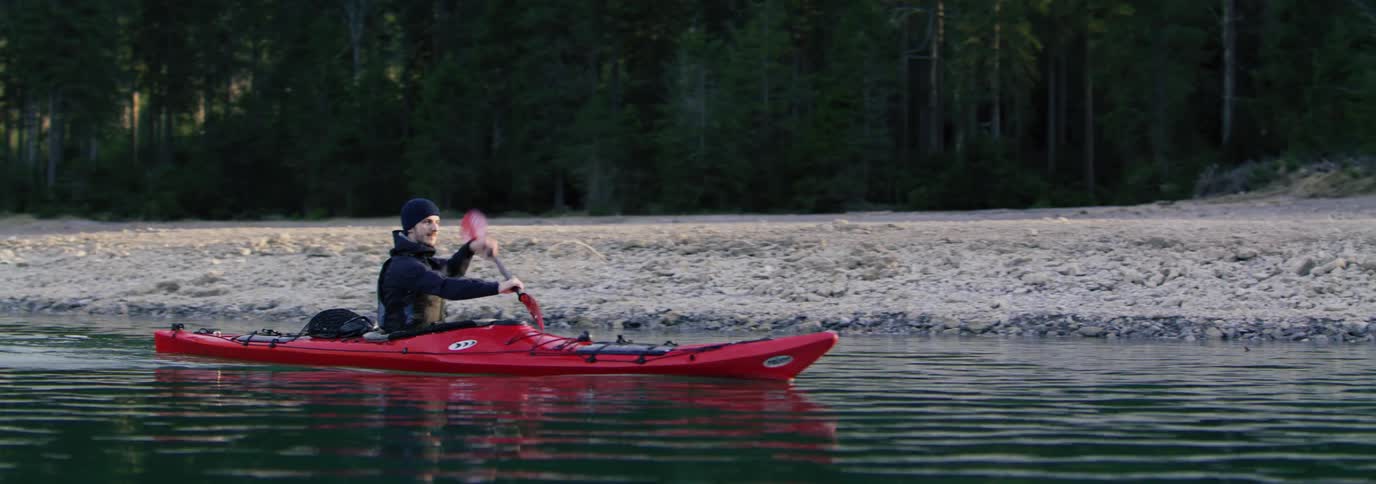 Man paddling a red kayak in calm water
