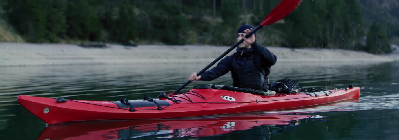 A man is rowing his kayak past the shore