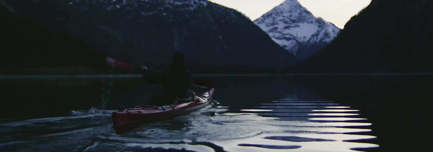 A man is rowing his boat by the mountains