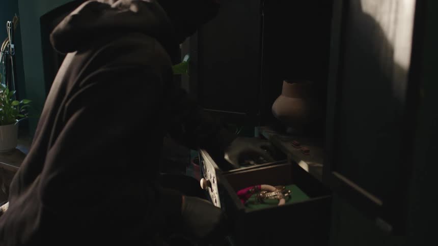 A burglar steals items out of a drawer in a room