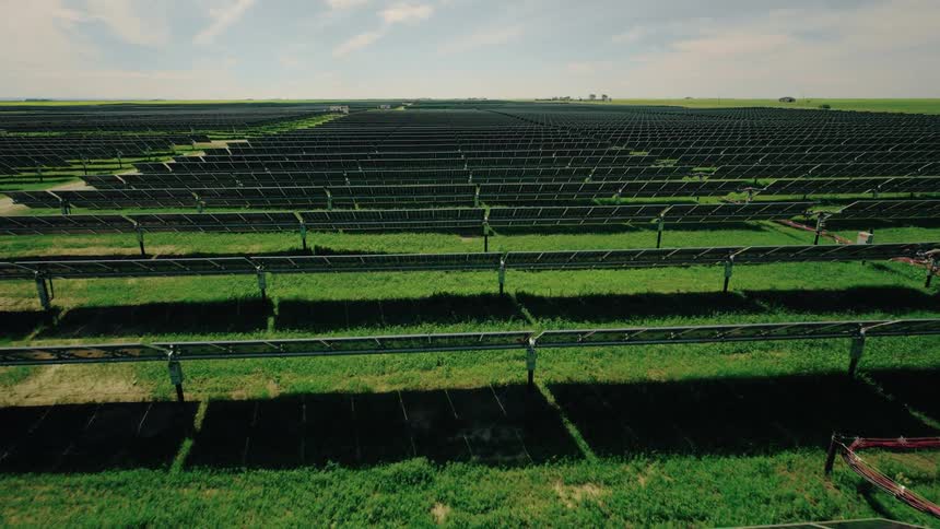 Slow moving aerial view of a green field with solar panels