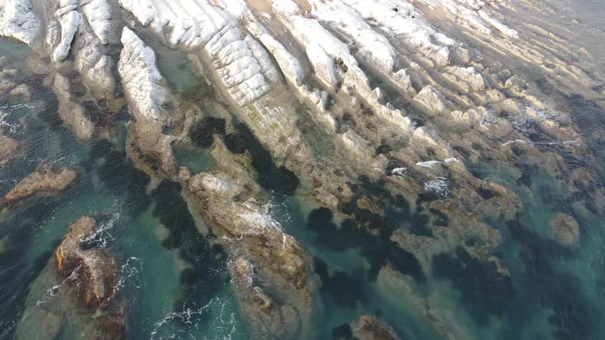 Aerial view of blue waters lapping at a rocky shore