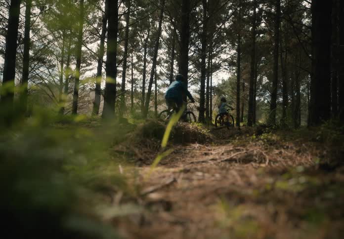 Two people ride their bikes into the forest