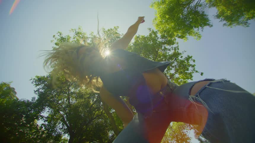 Sun glares down onto a blonde woman dancing outside under the trees on a summer day