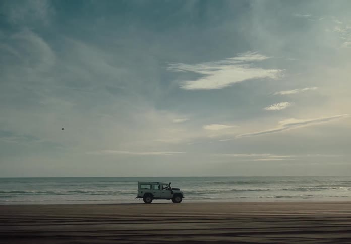 Jeep drives along the beach paralleling the shoreline on a cloudy day