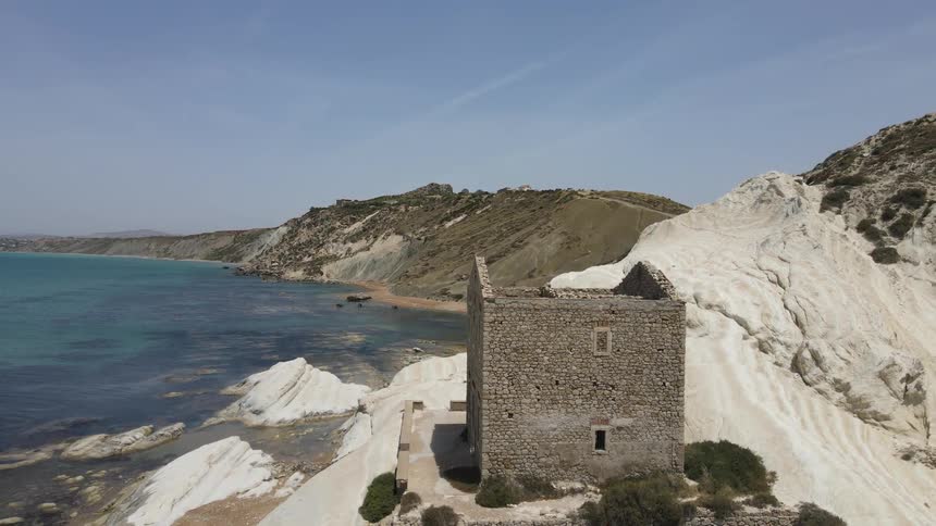 An ancient stone building situated on a scenic rocky coastline overlooking the ocean