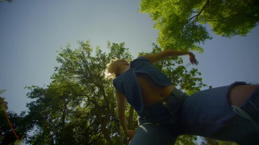 A woman dances outdoors wearing denim with sunlight filtering through tree leaves