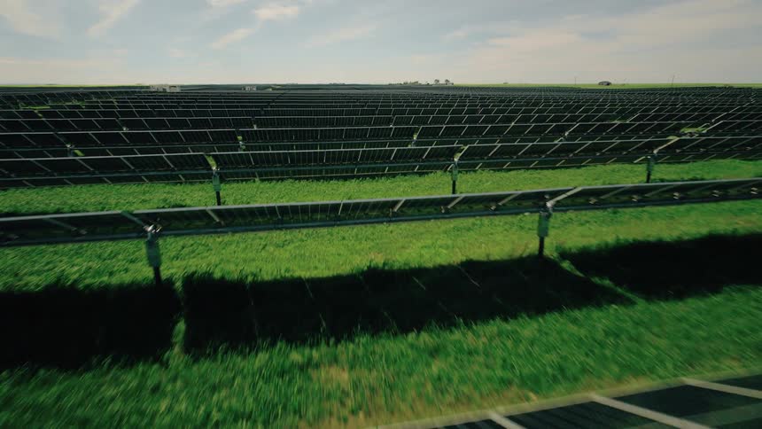 Flying over single-axis tracker solar panels on a green field