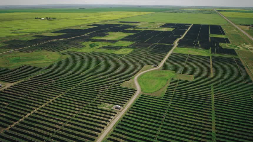 Aerial dolly in over single axis solar panels in a vast field