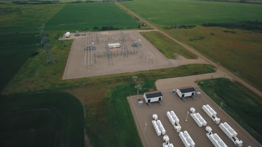 Aerial view of a fenced facility with large white industrial batteries arranged in rows
