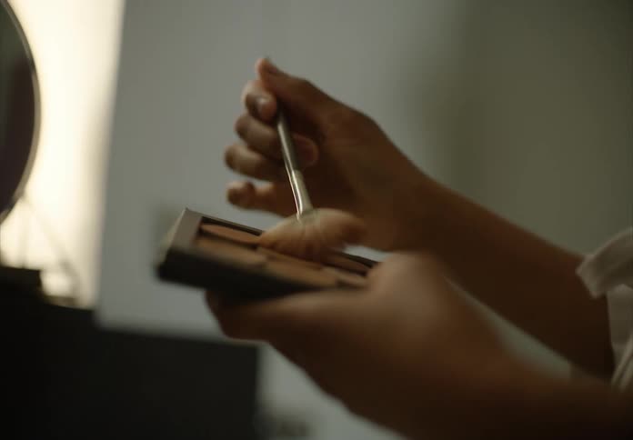 Woman hand holding a makeup palette and applying makeup in front of the mirror