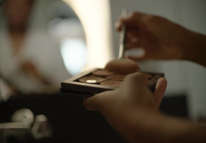 Woman holding a makeup palette and putting on makeup