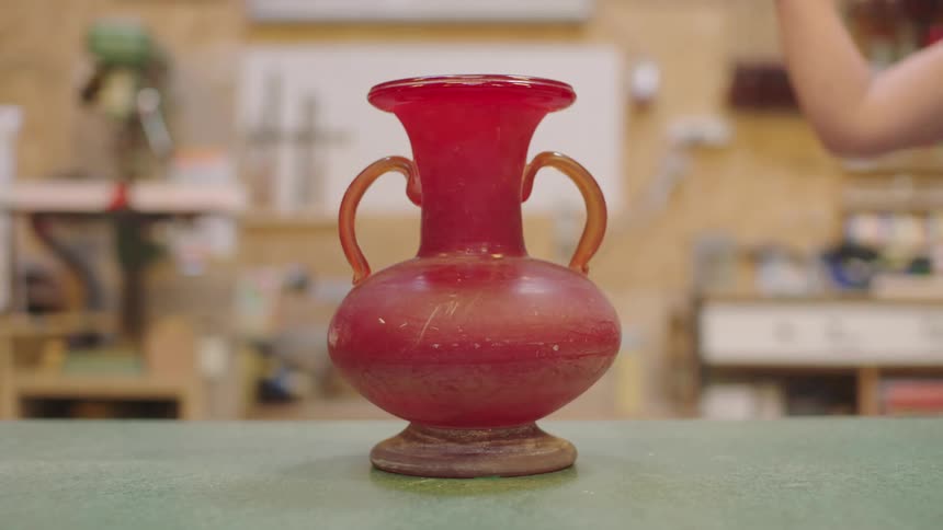 A closeup of a red vase being smashed with a hammer as the pieces shatter