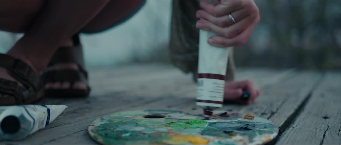A persons hands squeeze colorful paint from a tube onto a palette outdoors