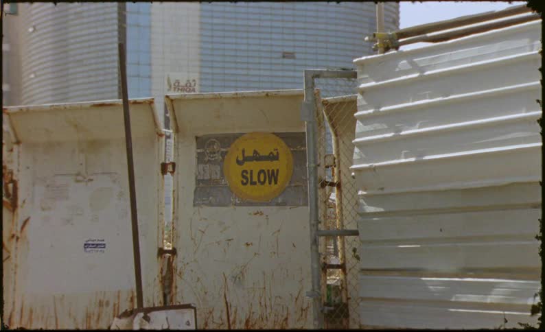 A weathered yellow sign with the word slow in black letters affixed to a rusty metal wall