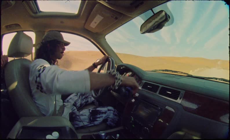 A man in a cap driving a car in a region with sand on the ground