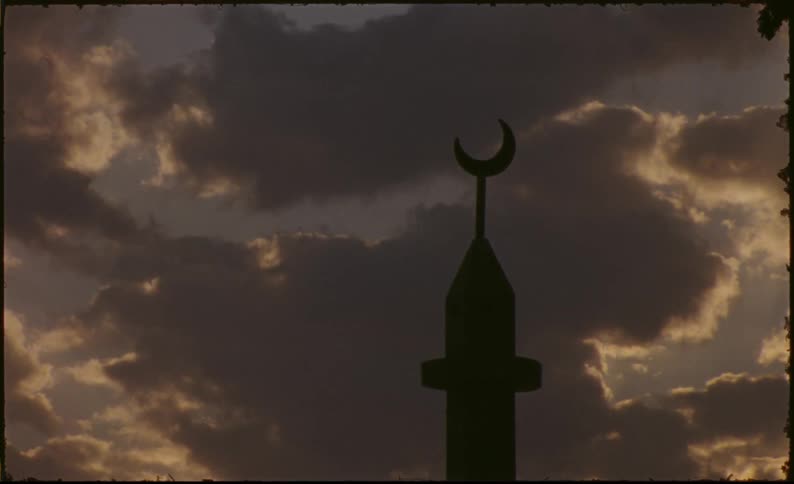 A mosques minaret against a dramatic sky with clouds highlighted by the setting or rising sun