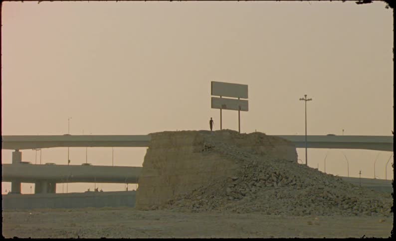 A person walking on a dirt embankment with a sign and behind there is a highway with cars passing by