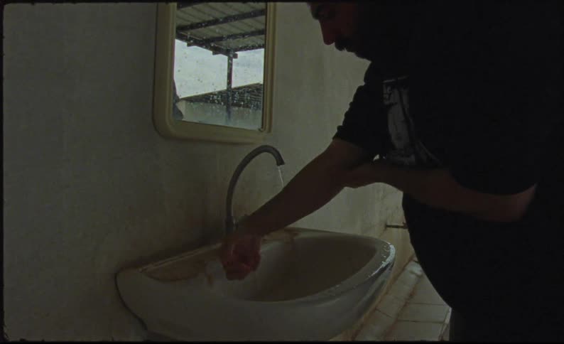Man washes up at a sink on an exterior building wall