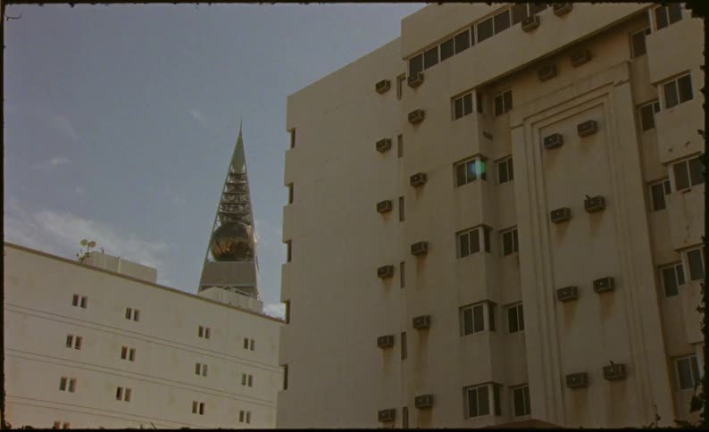 A beige building with several windows and a pointed tower on the left side