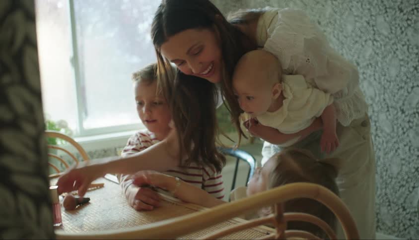 A woman holding her baby on her lap and there is a little boy and a little girl next to her and they are all looking at a table and are happy