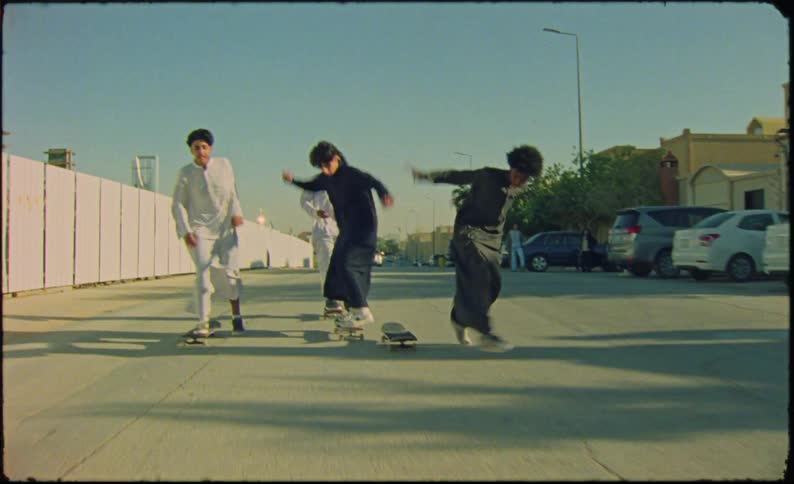 A group of teenagers all wearing robes skateboarding on the neighborhood streets