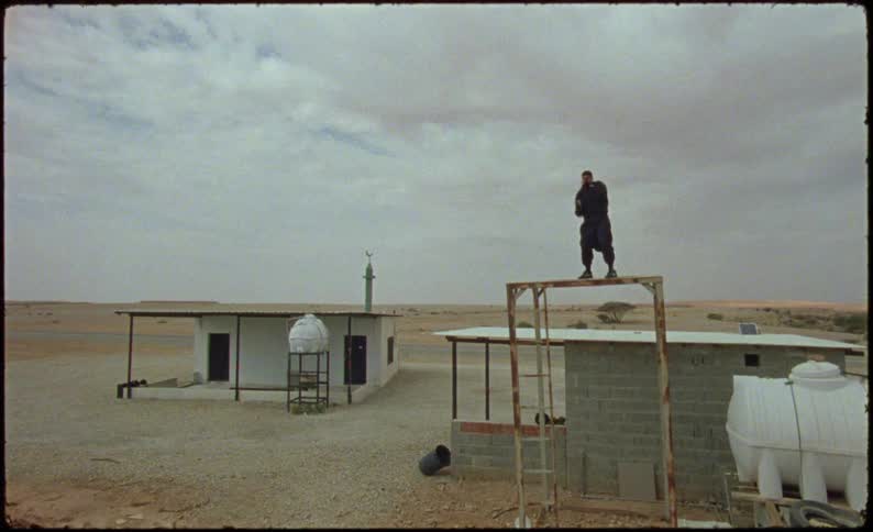 A man practices boxing while standing over a metallic structure in the desert