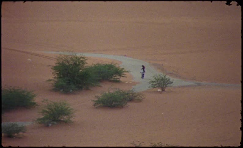 View from a distance of a man walking along a road in a place with desert dunes