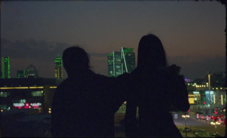 Silhouette of two women on terrace overlooking illuminated buildings at night in a metropolis