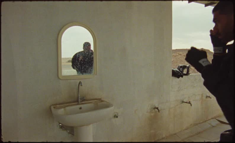 A young man boxing in front of a mirror on a run down house in the desert