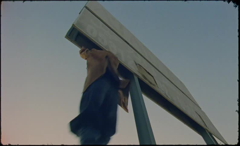 The male in the yellow jacket jumps up anhd grabs a billboard and starts swinging back and forthhe then lets go and lands in front of where he started