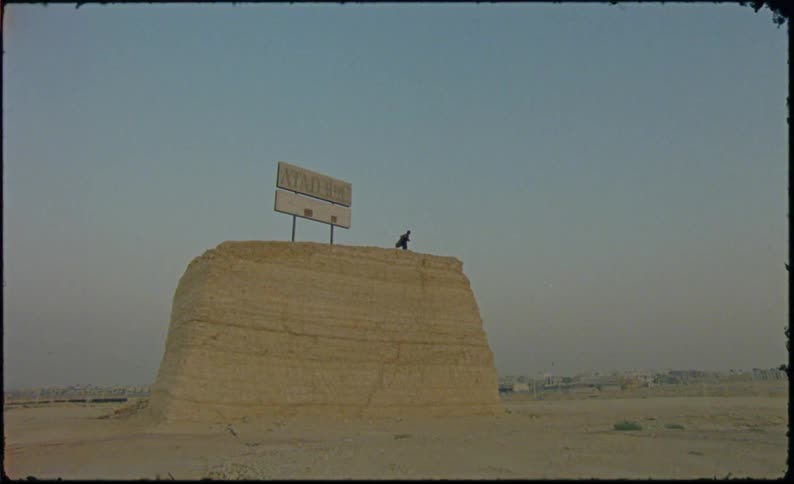 Person on a rock hill next to a billboard sign