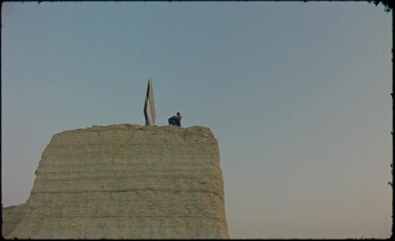 Person on top of a stone hill throwing a boot and a denim jacket
