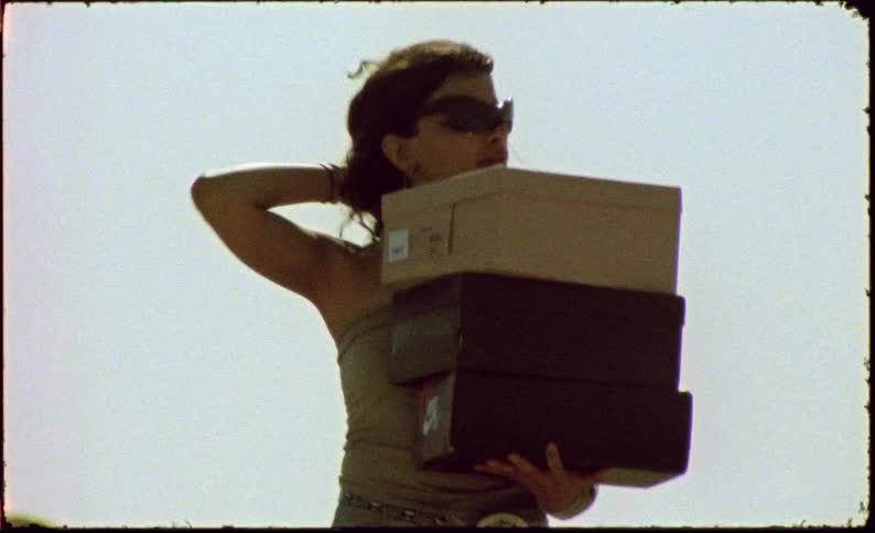 Woman walking on a deserted asphalt road holding shoe boxes