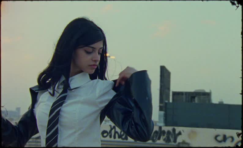 Teenage girls put jackets on while standing on a roof overlooking the city