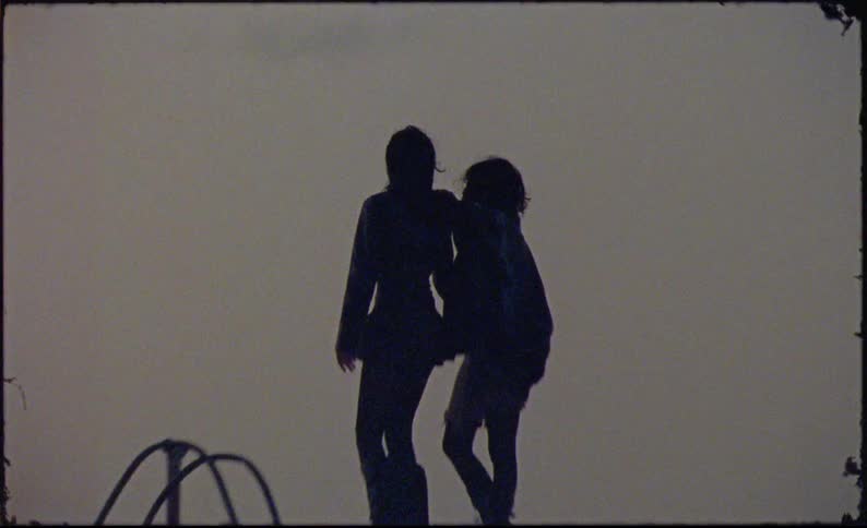 Two girls are standing and hugging each other and they are both dressed in black clothes