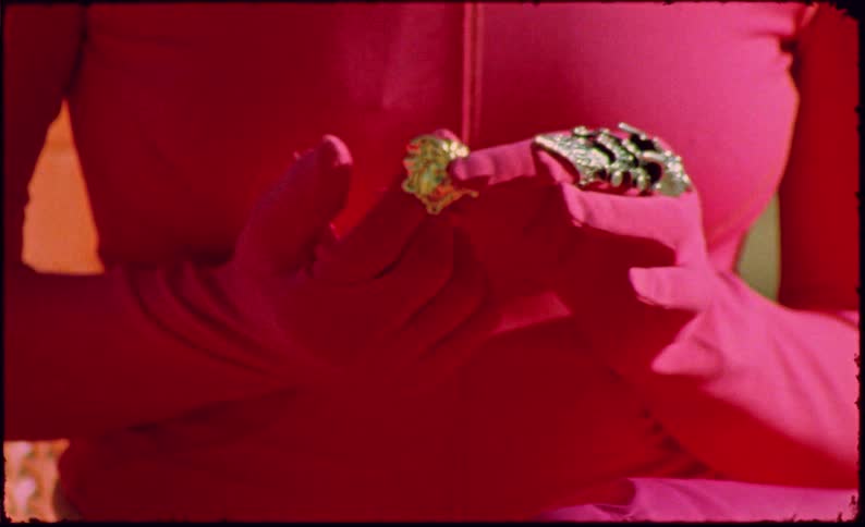 A woman in a bright pink outfit sits on an orange chair examining a small object in her hands
