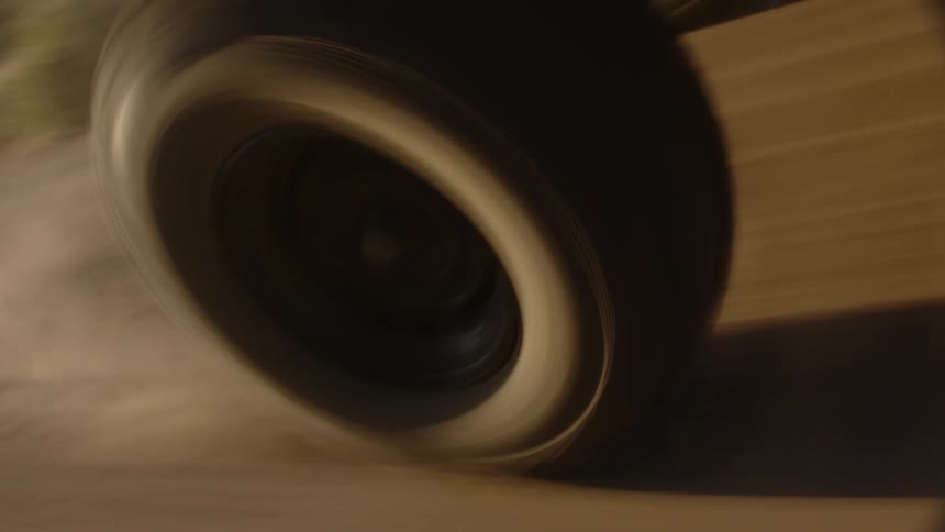 A large tire spins and kicks up dirt on a remote rural dirt road